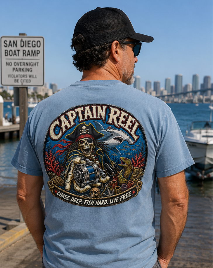 Man with curly hair, wearing a black cap, sunglasses, and a Captain Reel t-shirt, standing near a marina with boats and city skyline in the background.