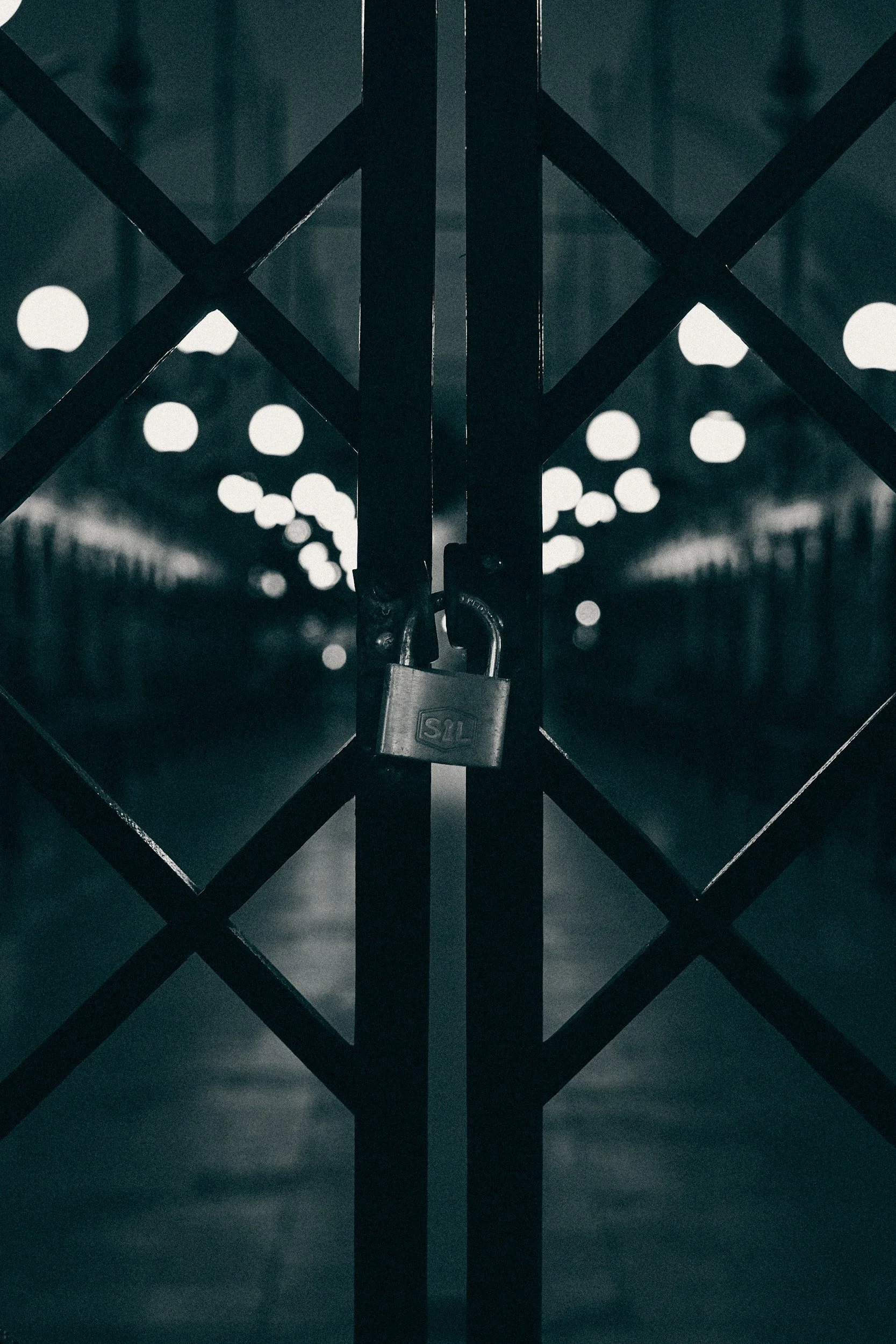 A black padlock attached to a metal chain link fence, with a blurred background of round light spots.