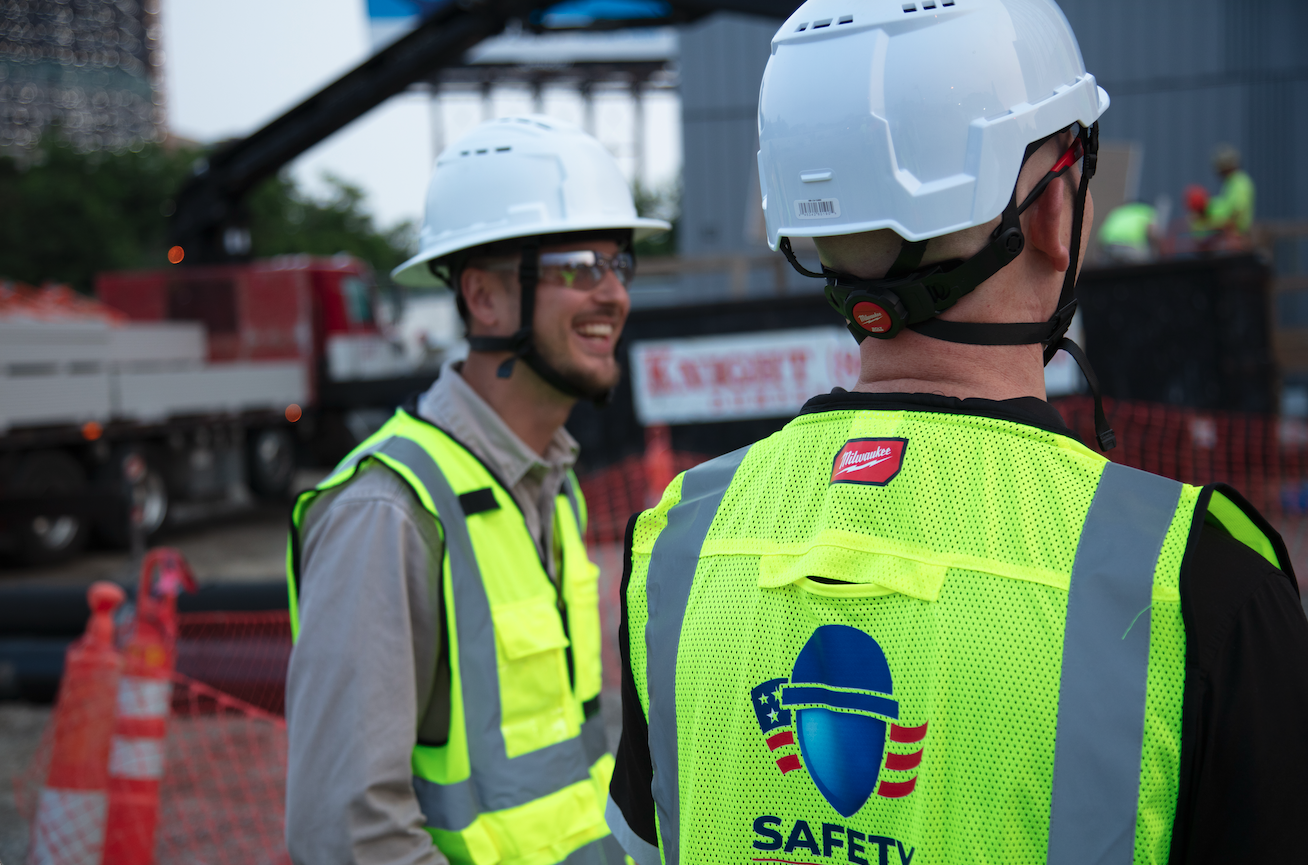Construction workers in safety vests and helmets on a construction site, engaged in conversation.