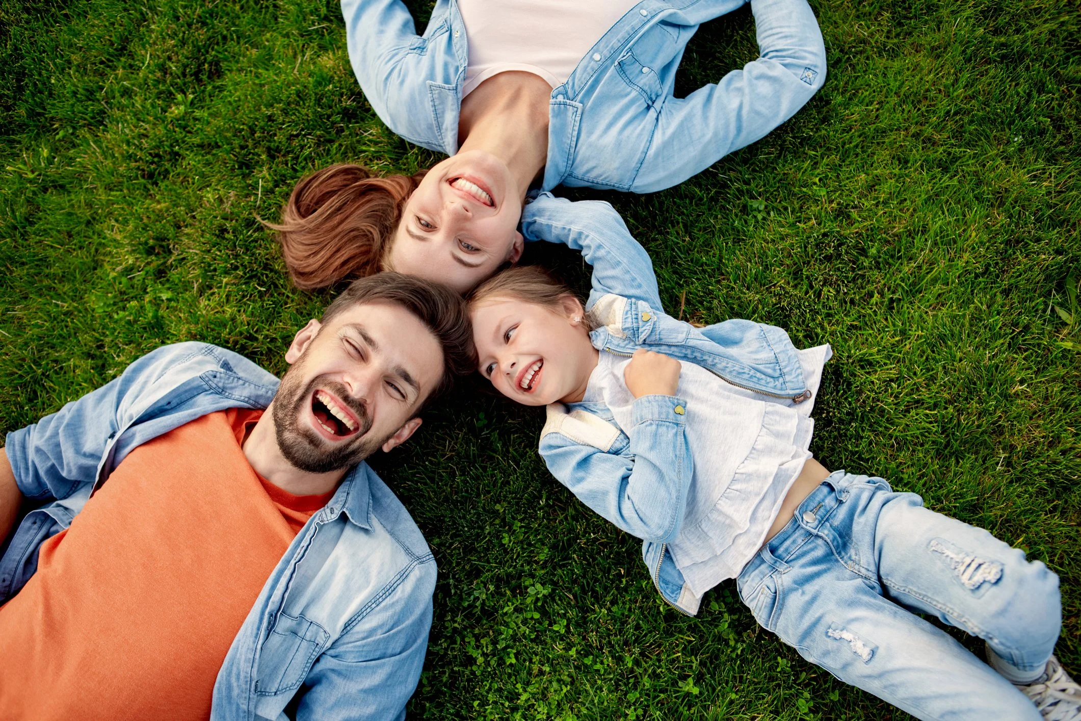 A family of four lying on the grass and smiling.