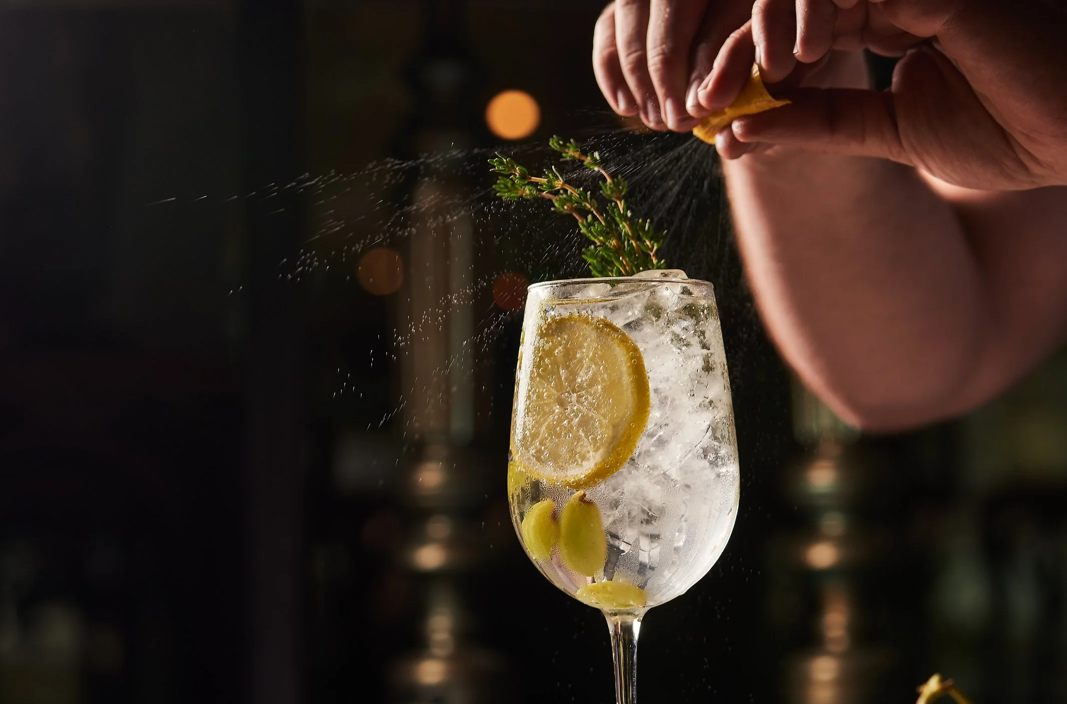 A cocktail glass with ice, lemon slices, and green olives, garnished with a sprig of thyme. 