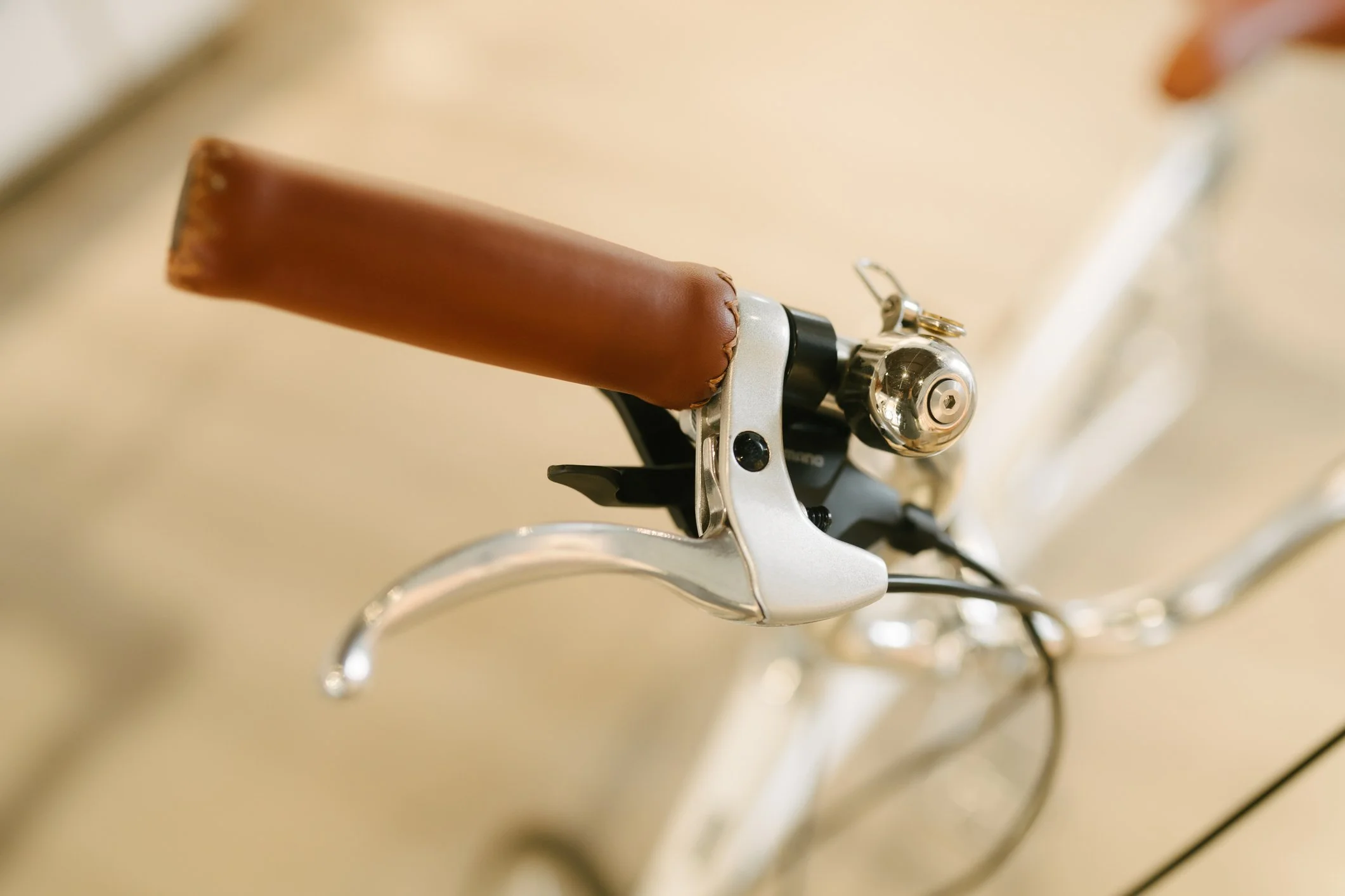 Close-up of a bicycle handlebar with a brown leather grip and a silver brake lever.