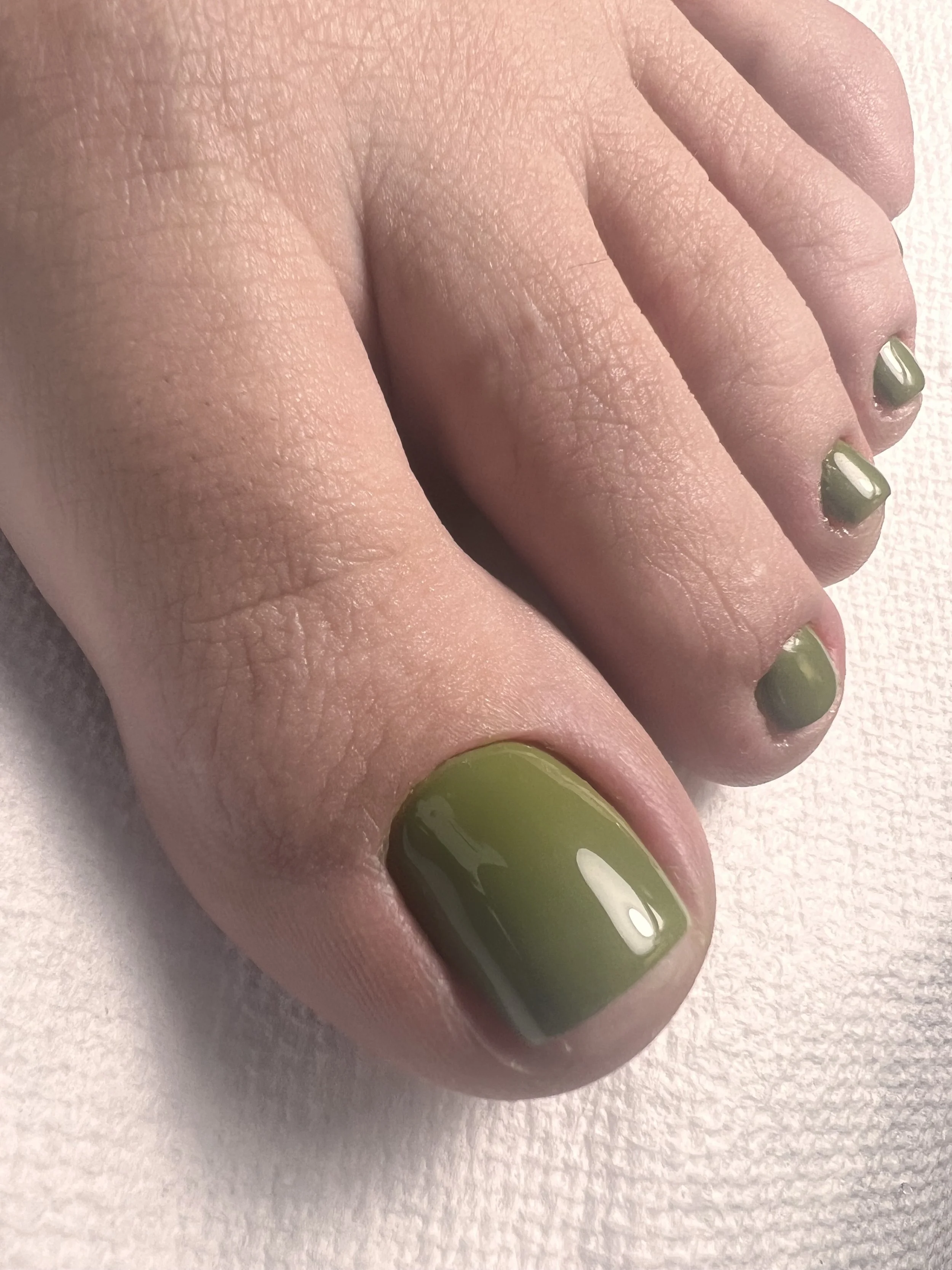 Close-up of a hand with nails painted in a matte army green color, showing the fingers and part of the palm, against a light background.