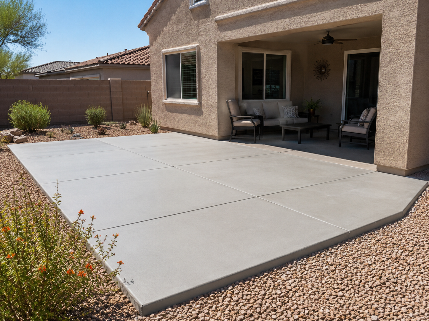 Backyard patio with a concrete slab, patio furniture, and desert landscaping.