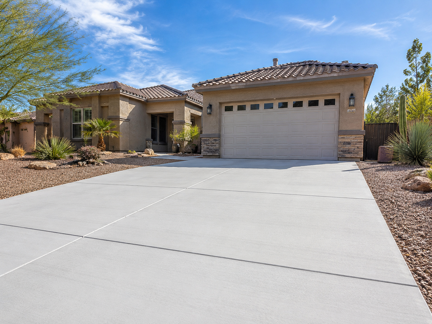 Front view of a beige single-story house with a two-car garage, desert landscaping, and a blue sky.