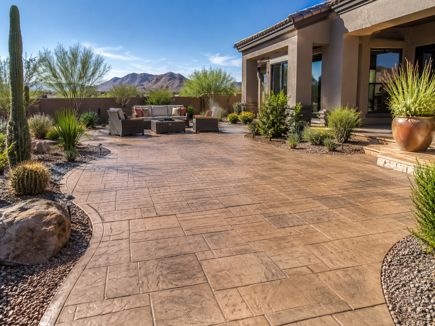 A backyard patio with stamped concrete flooring, desert plants, and mountain views in the background.