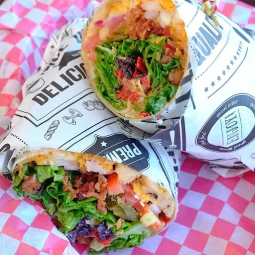 Two wrapped burritos with visible ingredients including lettuce, tomato, cheese, and ground meat, resting on a red and white checkered surface.