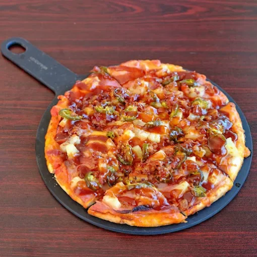 A freshly baked pizza with toppings including ground meat, green bell peppers, and melted cheese on a small black pizza tray.