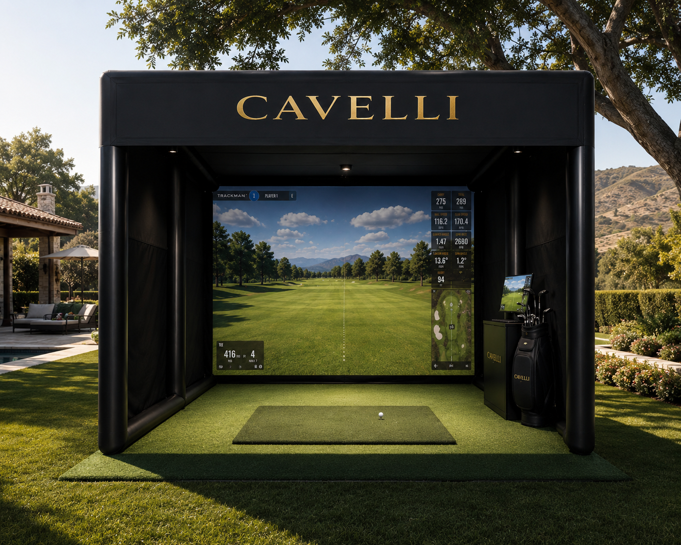 A golf simulator setup labeled Cavelli with a virtual golf course on the screen, surrounded by golf clubs and a small platform with a golf ball in the foreground, outdoors on a green lawn with trees and a house in the background.
