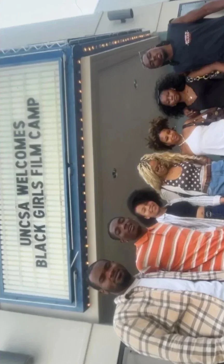 Group of black film students, women and men, standing in front of a sign that reads 'Uncsa welcomes Black girls film camp'
