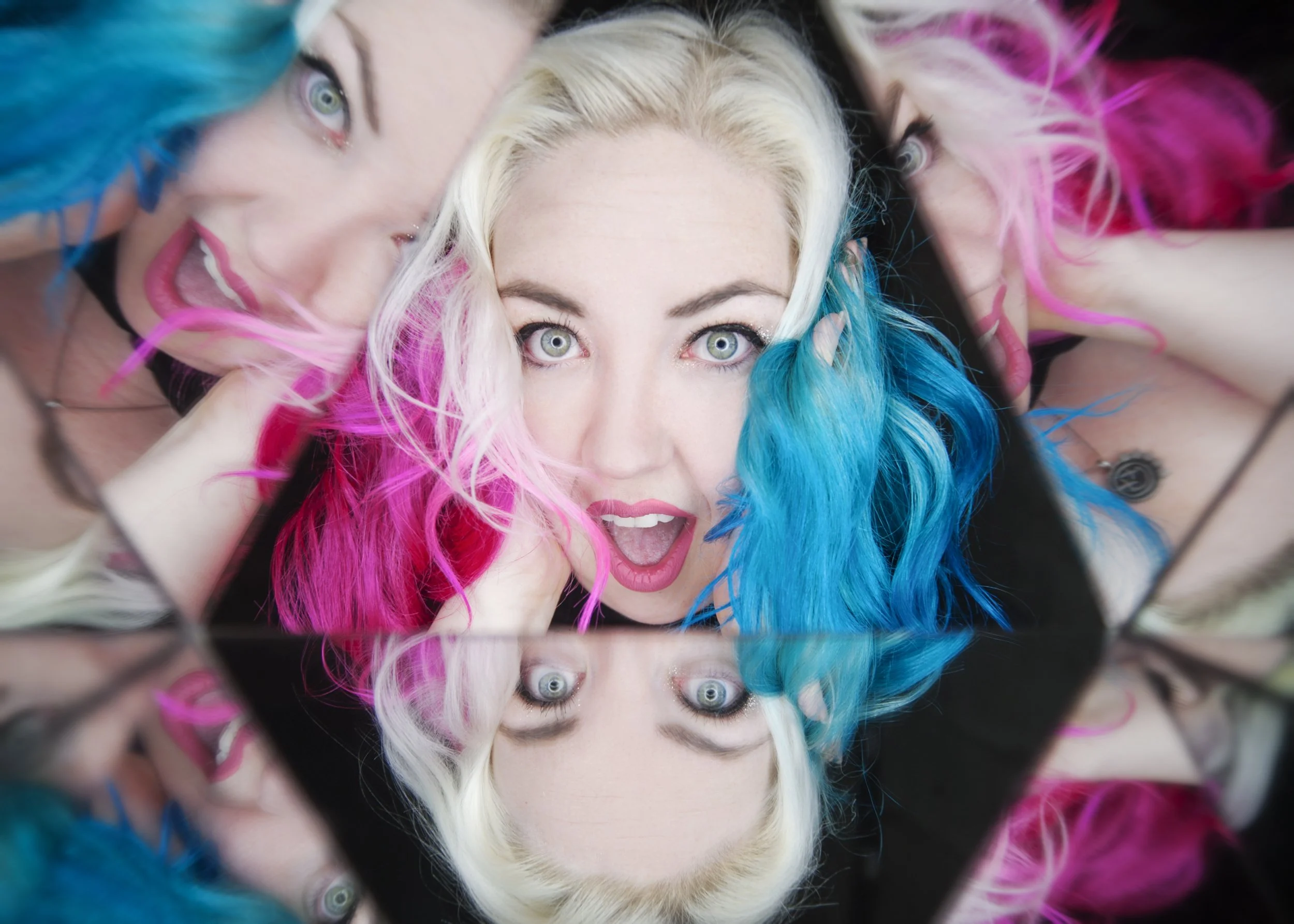 Close-up of a person with multicolored hair (blue, pink, blond with blue tips), looking up at the camera with surprised expressions.