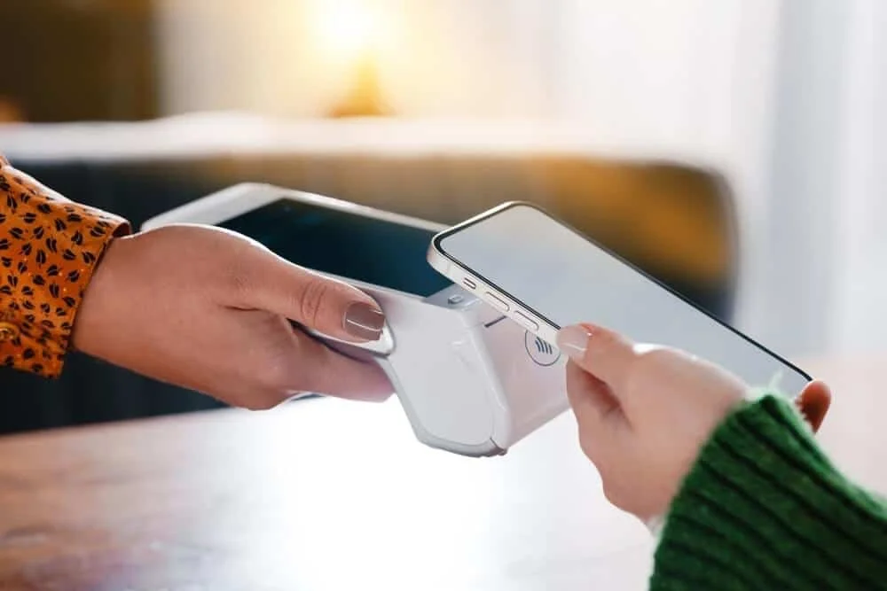 Person using a smartphone to make a contactless payment at a point-of-sale terminal.