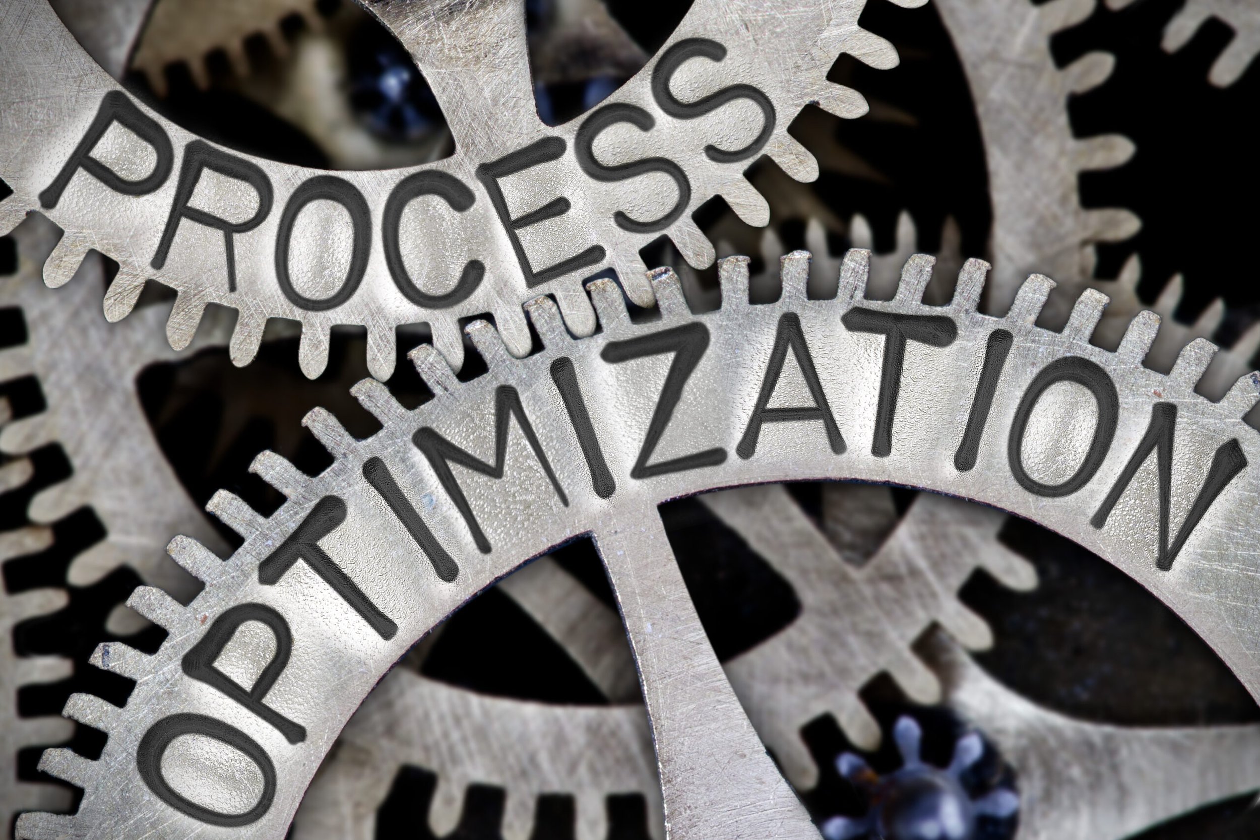 Close-up of metallic gears with the words 'PROCESS OPTIMIZATION' engraved on them.