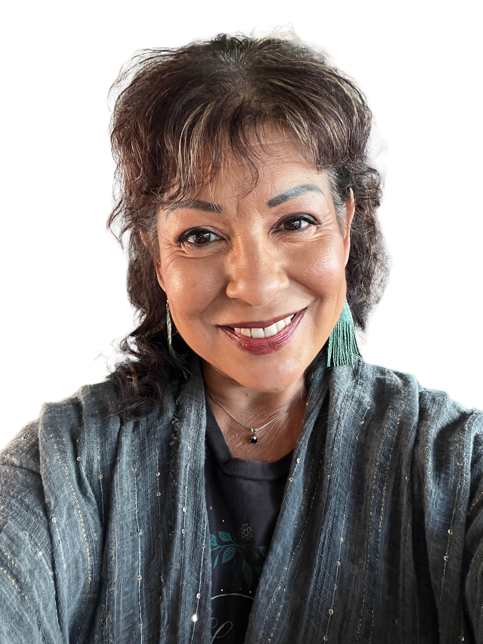 A smiling woman with short, wavy gray and black hair, wearing earrings, a pendant necklace, a dark shirt, and a gray, sparkly, long-sleeve jacket.