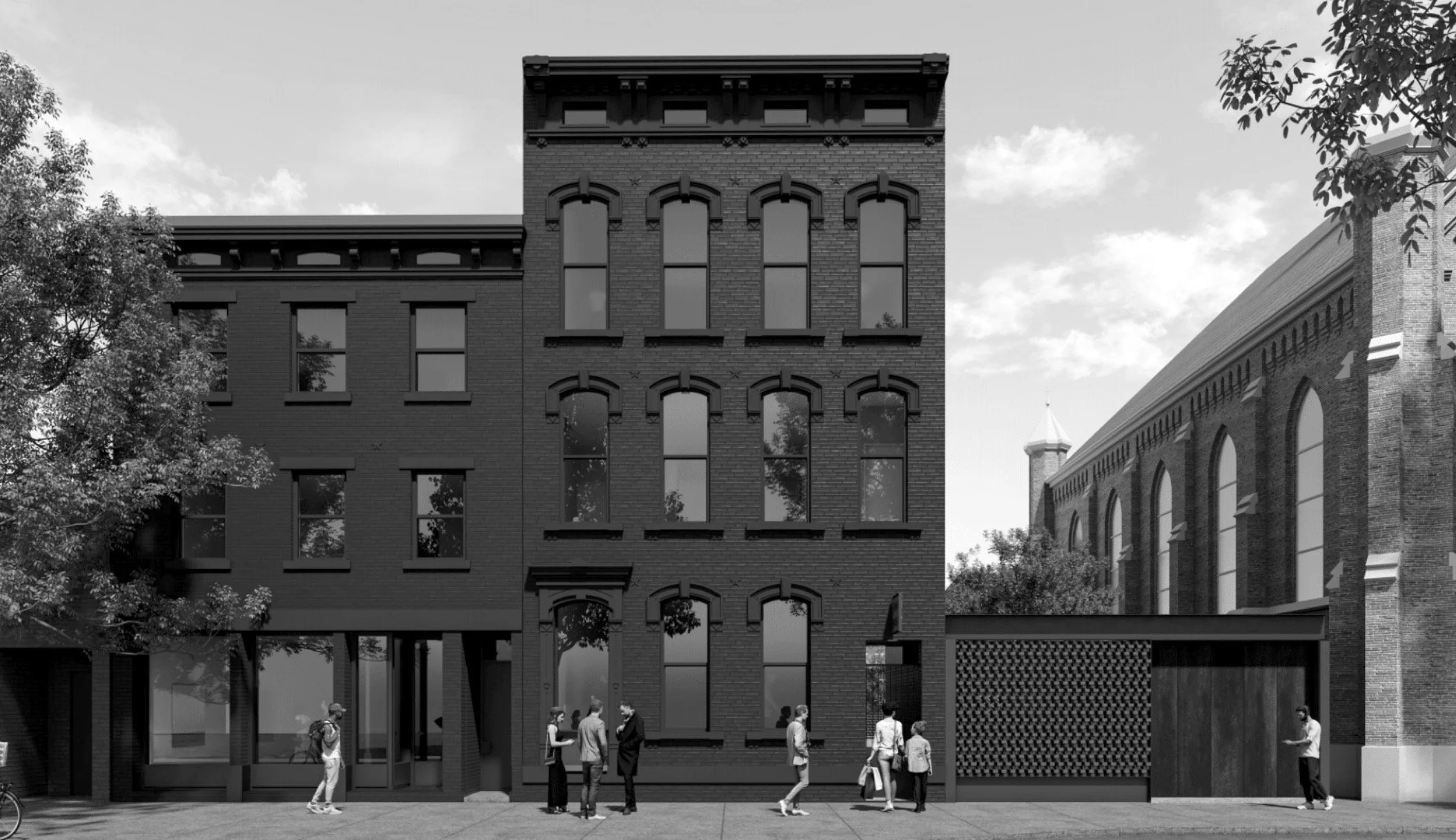 Black and white photo of a historic brick building with tall narrow windows and people walking along the sidewalk in front.