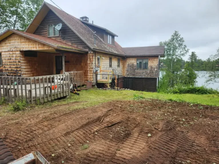 A house with a wooden trim exterior, located near a body of water, with construction or landscaping work happening in the yard.