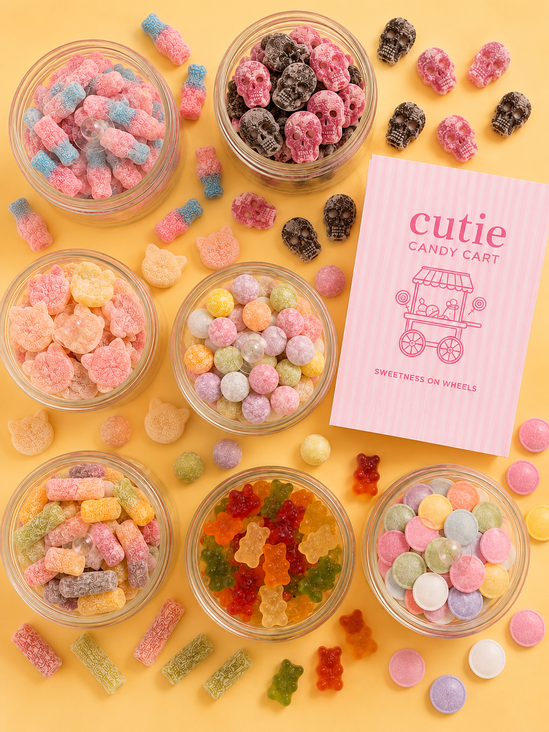 Colorful gummy candies and candy skulls in small glass bowls, with a pink privacy sign for 'Cutie Candy Cart' on a yellow background.
