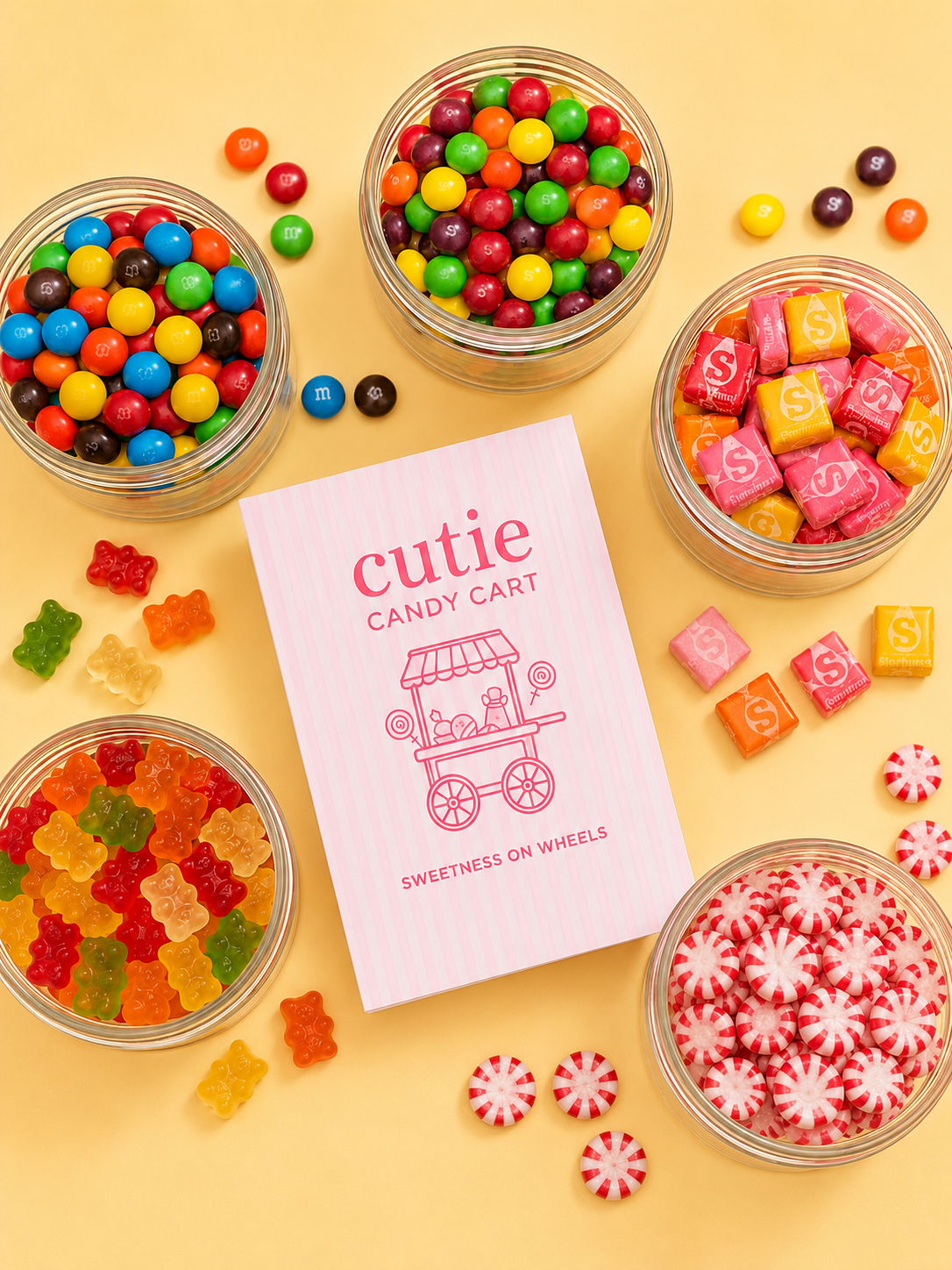 Various bowls of colorful candies including gumballs, gummy bears, wrapped caramels, and peppermint candies, with a pink-striped paper flyer for 'Cutie Candy Cart'.