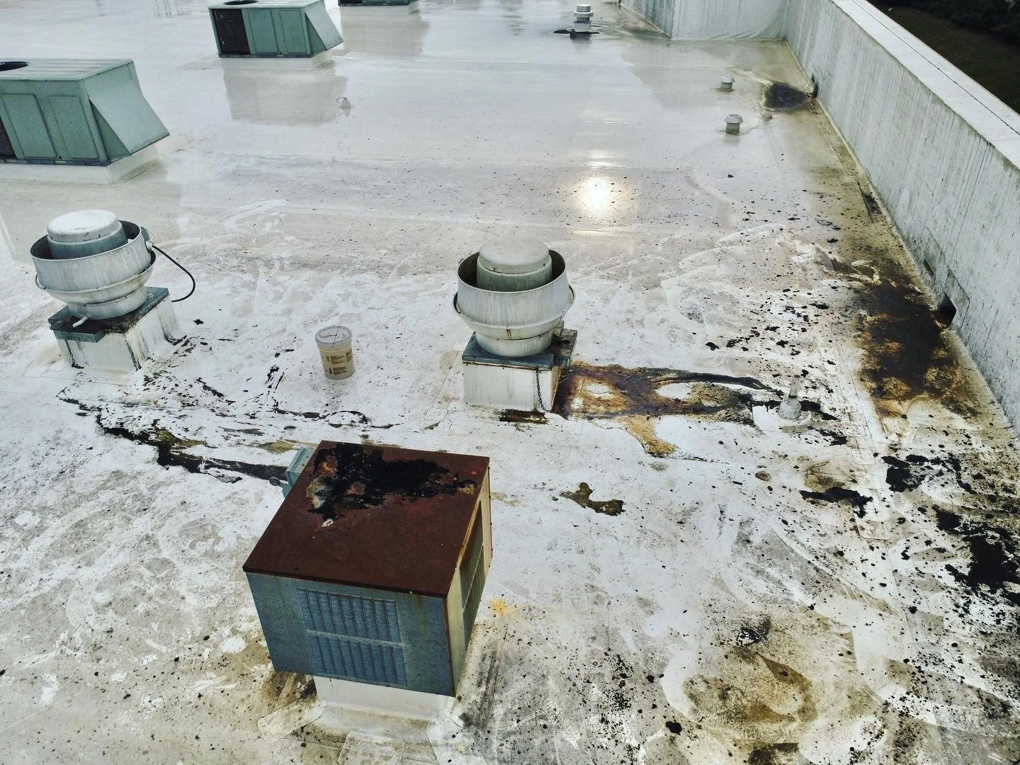 Deteriorated rooftop with vents and HVAC units, showing signs of water damage, corrosion, and accumulated dirt and debris.