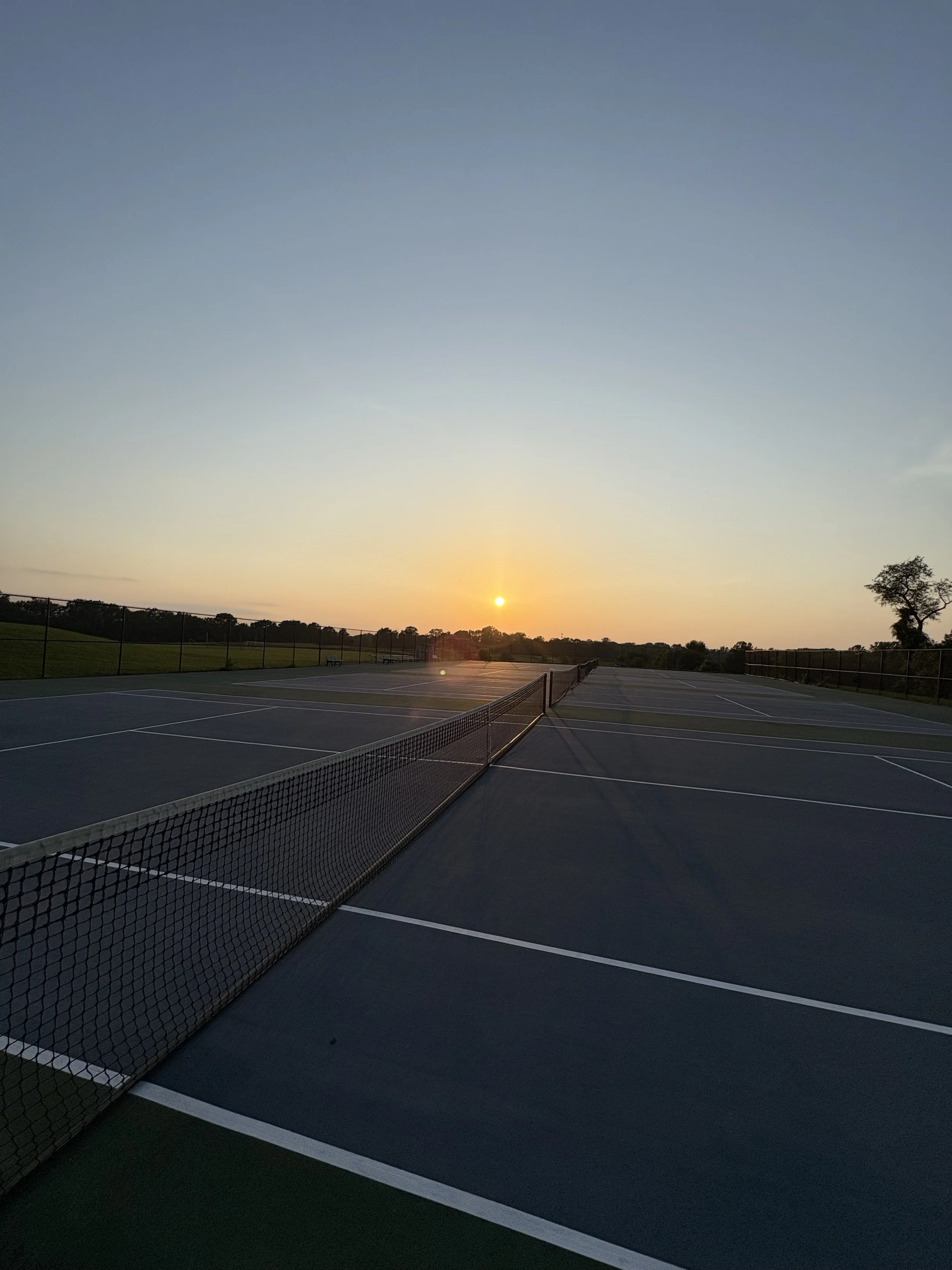 Empty tennis courts during sunset with the sun near the horizon and a clear sky.
