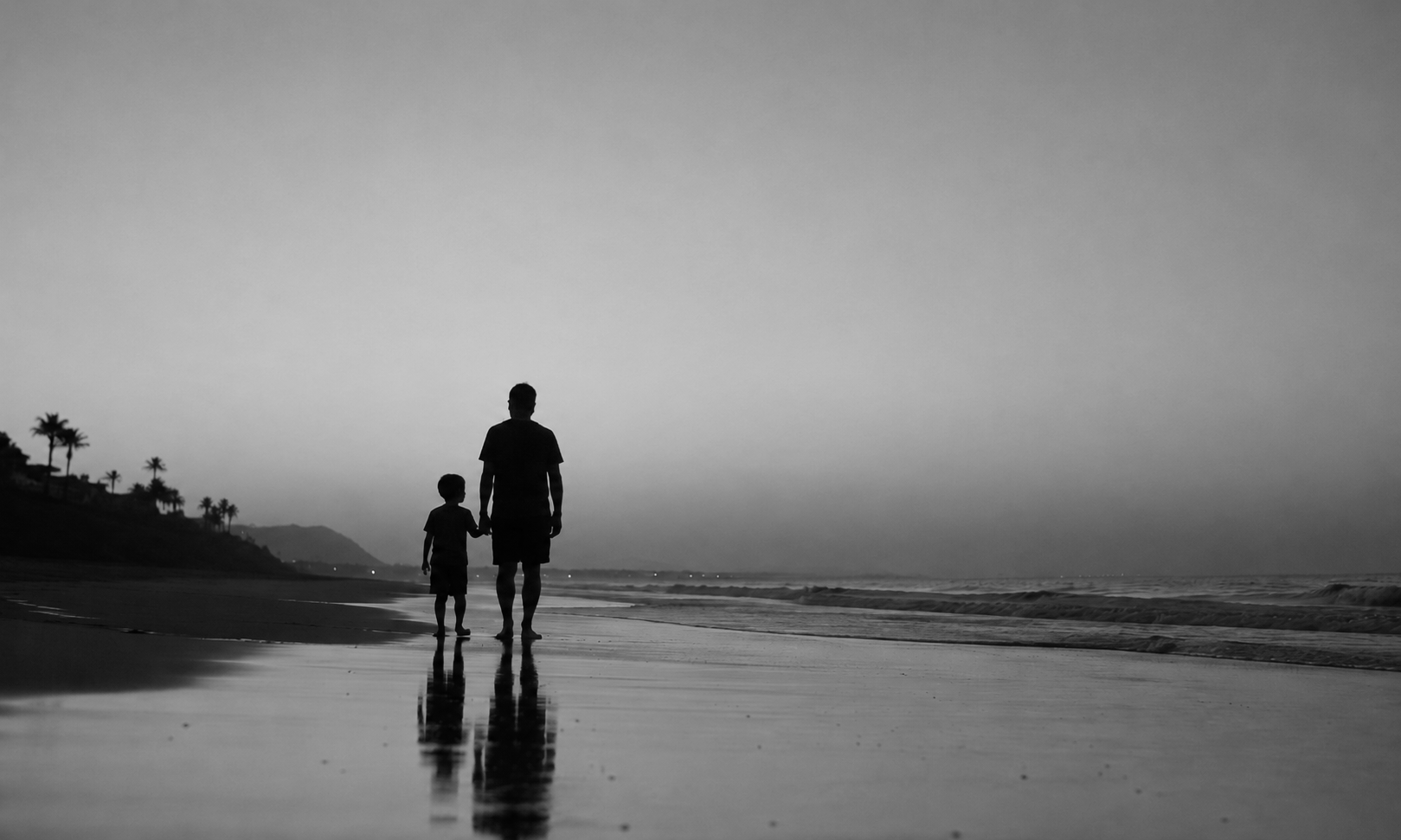 Silhouettes of a man and a child walking hand in hand on the beach at sunset or sunrise, with reflections visible on the wet sand and palm trees in the distance.