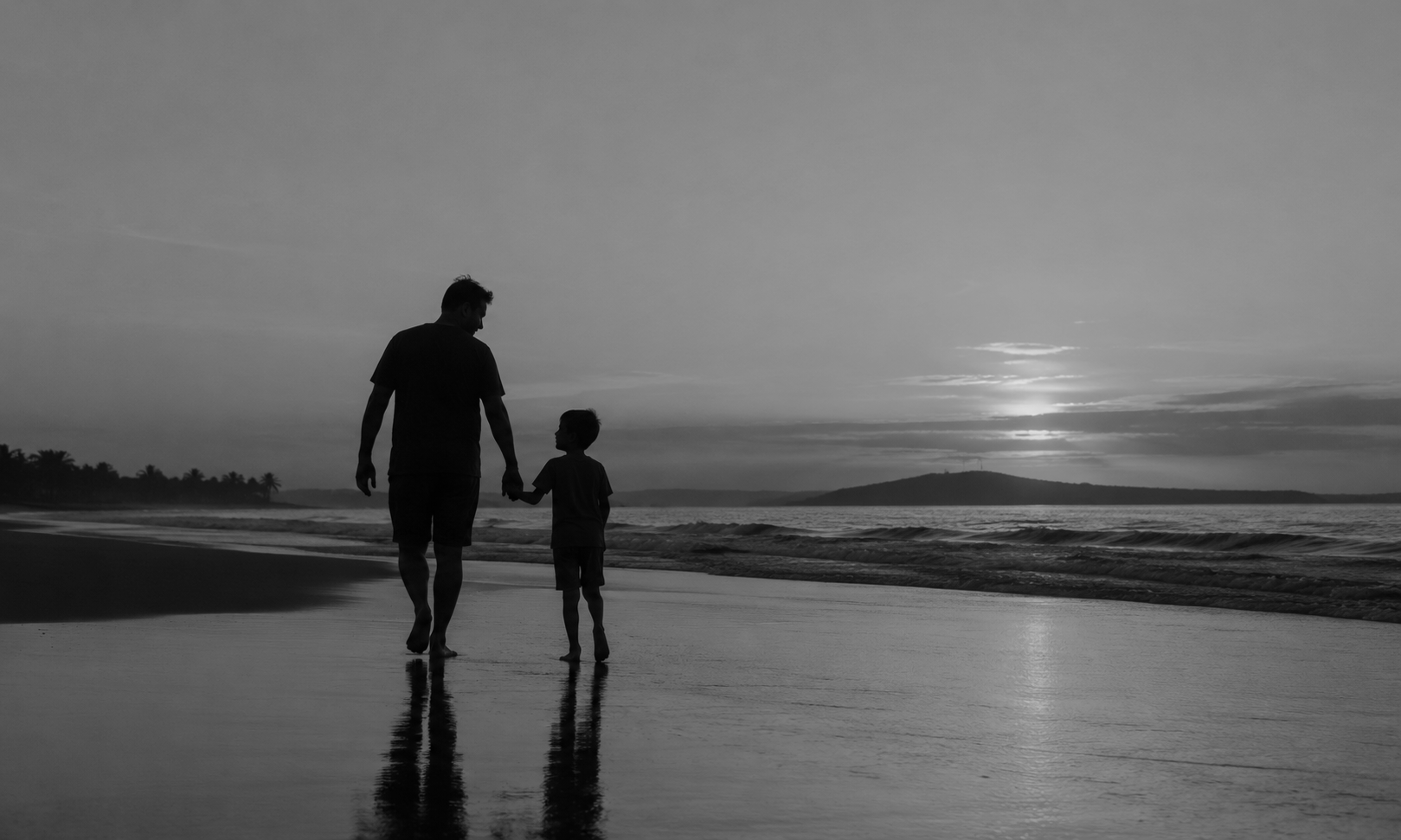 A silhouette of an adult and a child holding hands walking along the beach during sunset or sunrise, with the ocean waves and distant land visible.