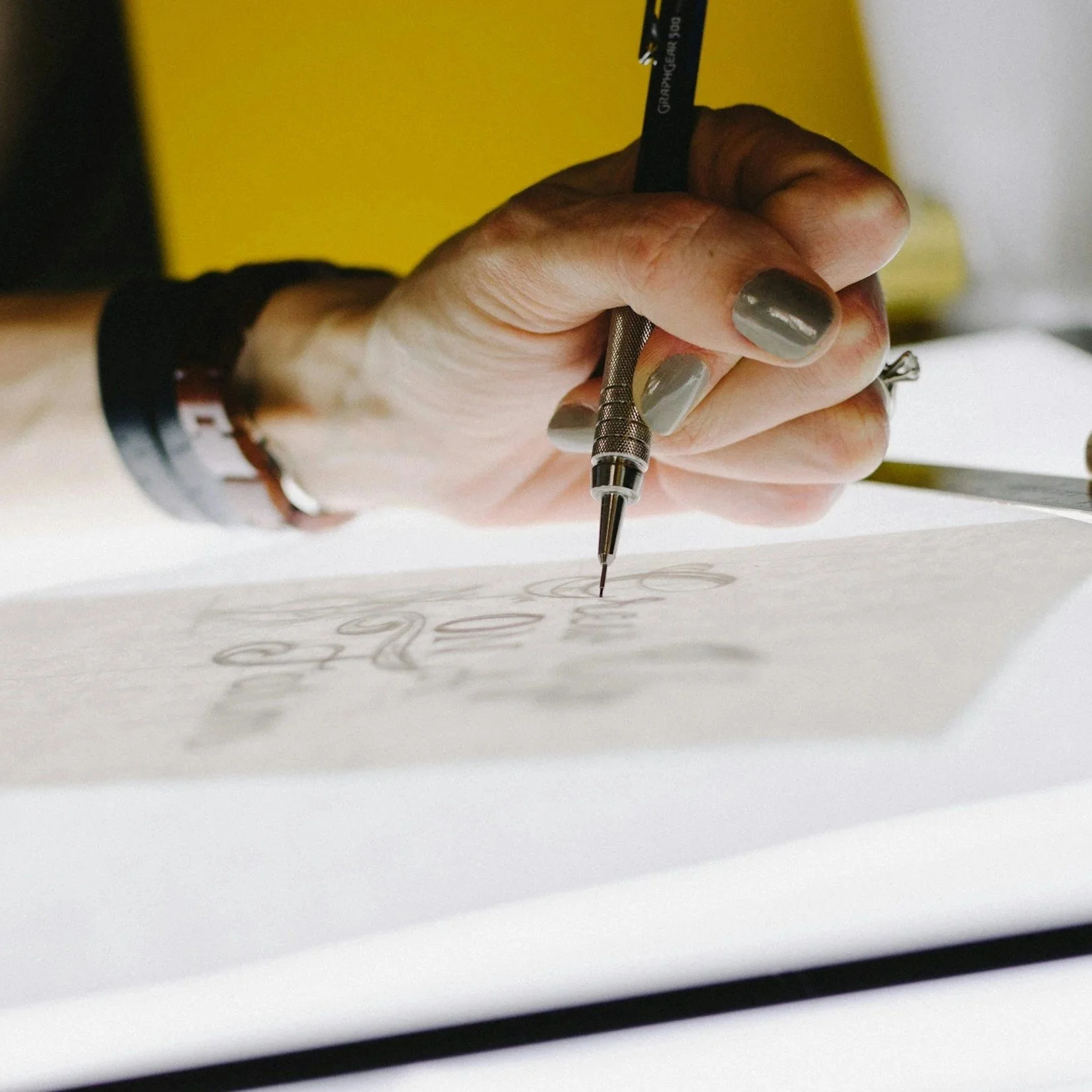Close-up of a person's hand writing with a black pen on a piece of paper, with a yellow background.