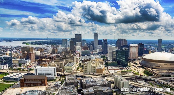 A panoramic view of a city skyline with tall buildings, a large stadium, and a partly cloudy sky.