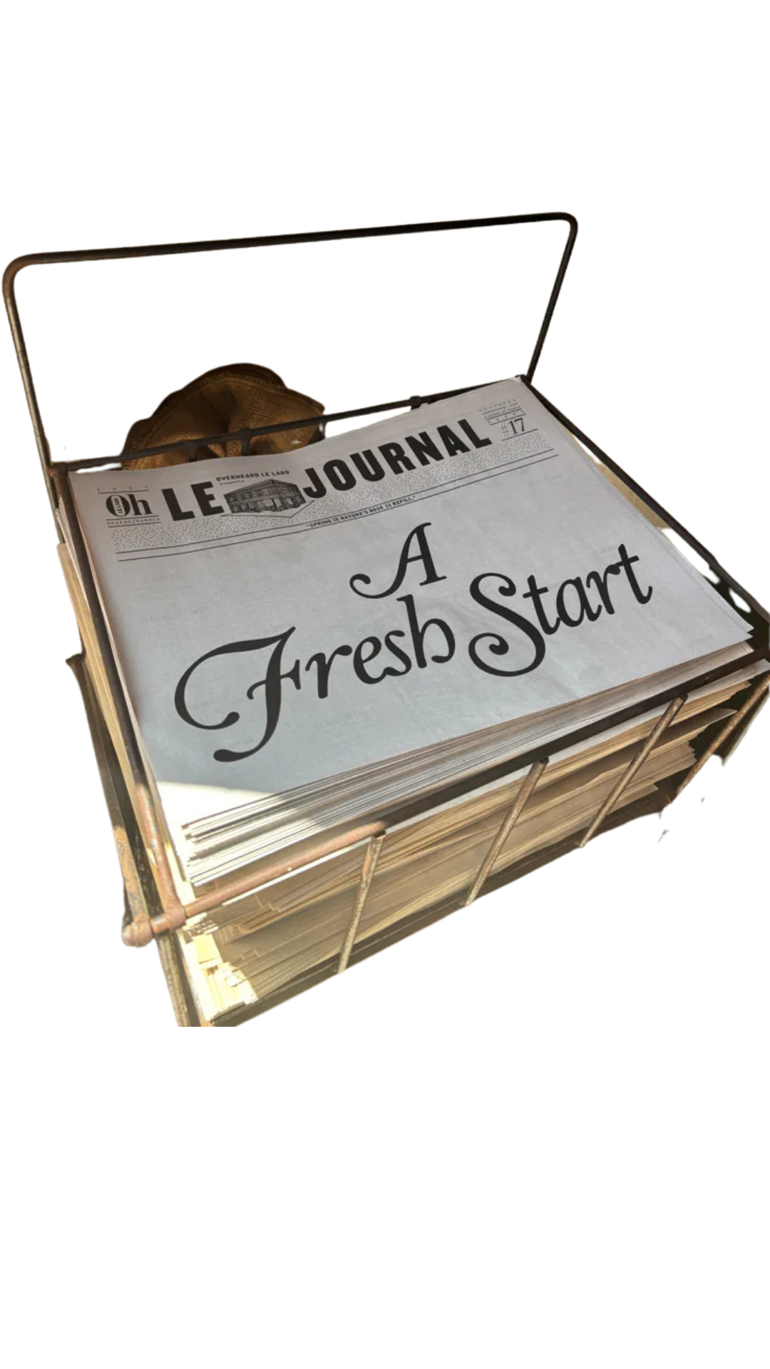 A vintage wire basket filled with newspapers, with a prominent headline reading 'A Fresh Start' in large cursive font.