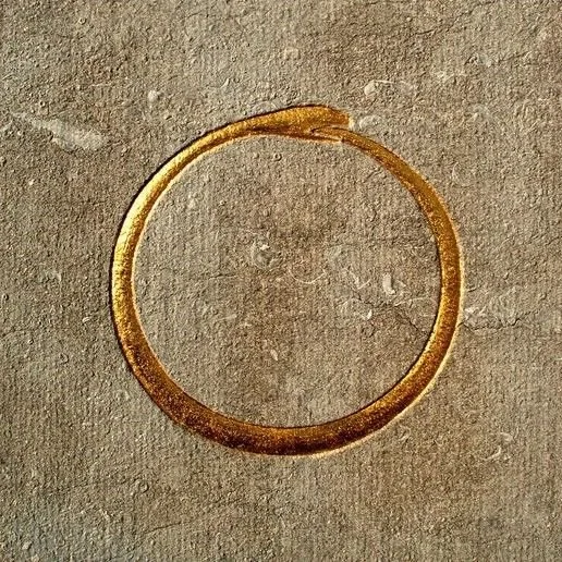 A simple gold ring placed on a textured beige surface.