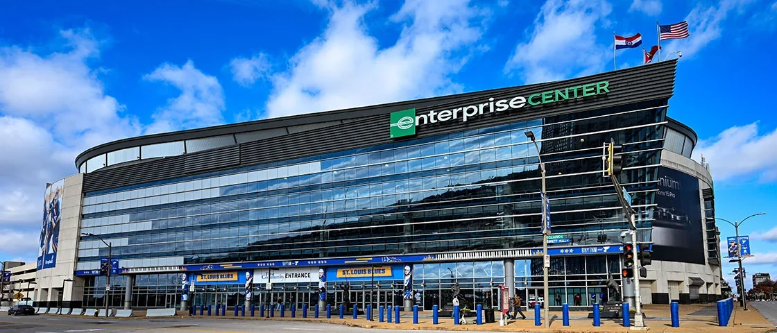Exterior of the Enterprise Center, a multi-story glass building with blue accents and flags on top, located in downtown St. Louis, Missouri.
