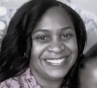 A smiling woman with long dark hair, wearing a patterned blouse.