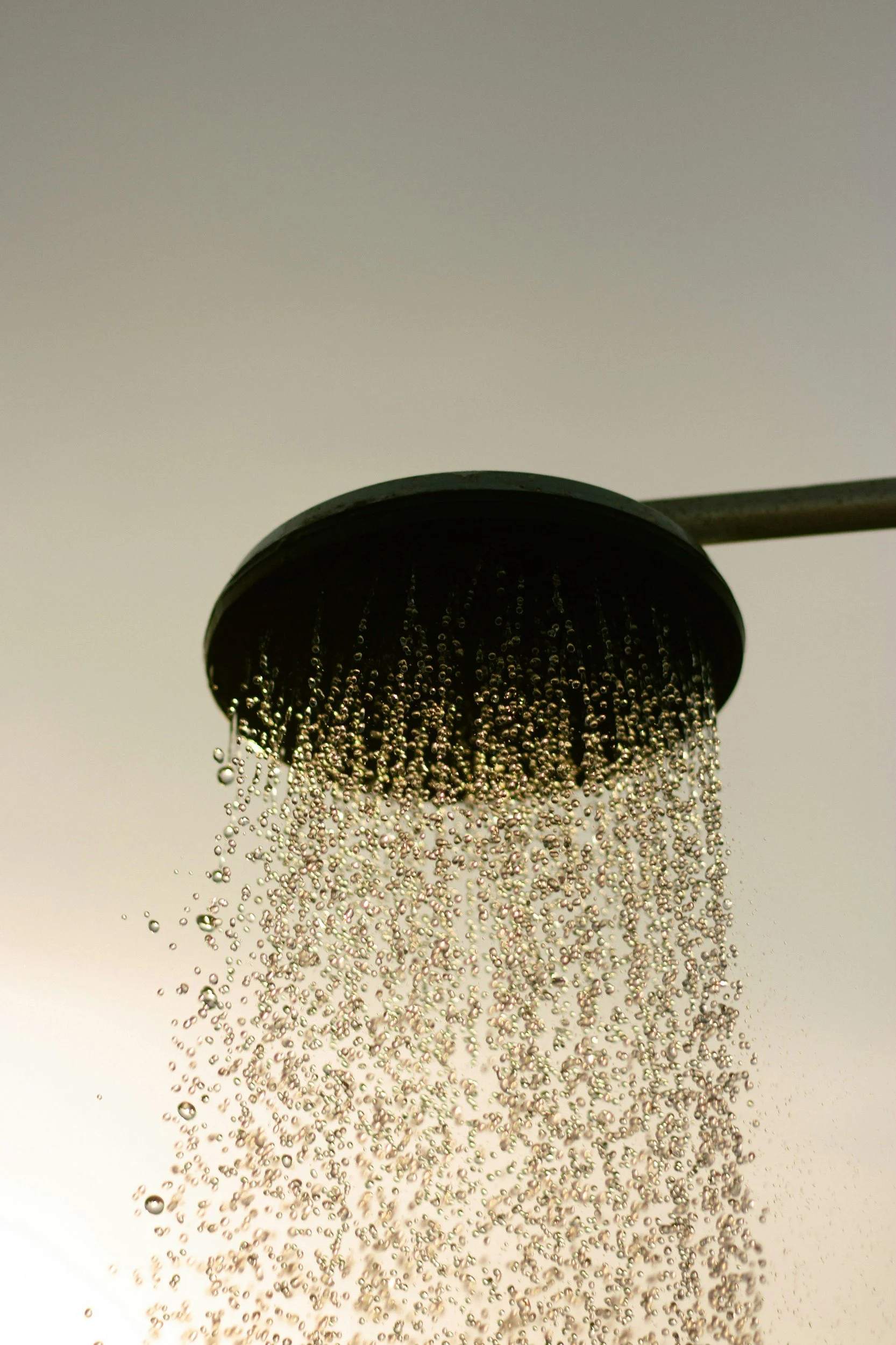 A shower head releasing water droplets against a plain background.