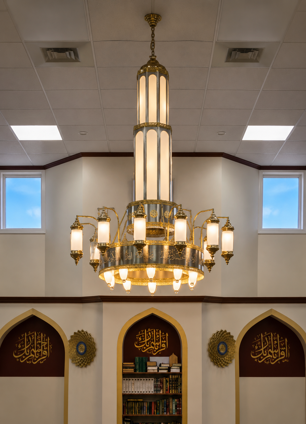 Inside a mosque showing a large decorative chandelier hanging from the ceiling and framed calligraphy on the wall.