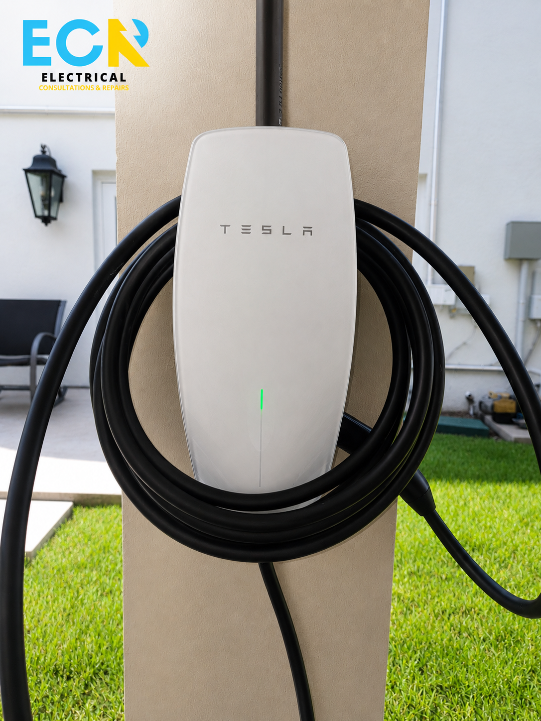Tesla electric vehicle charging station with black charging cables attached, set against a beige wall with a green lawn in the background.