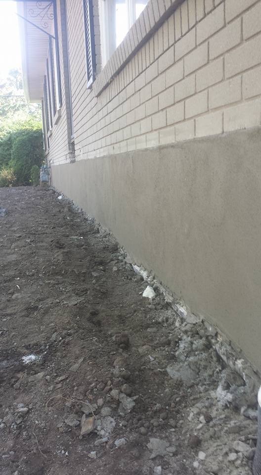 A view of a house exterior with a newly painted gray foundation wall and unpaved dirt ground in front.