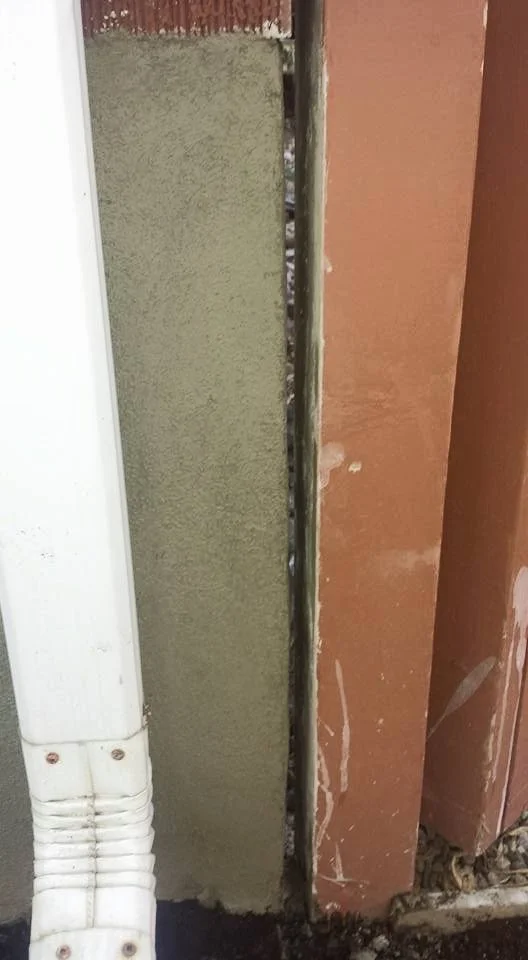 Close-up of a wall with a partially exposed electrical conduit or pipe between a green wall and a red wall, with some debris and dirt at the base.
