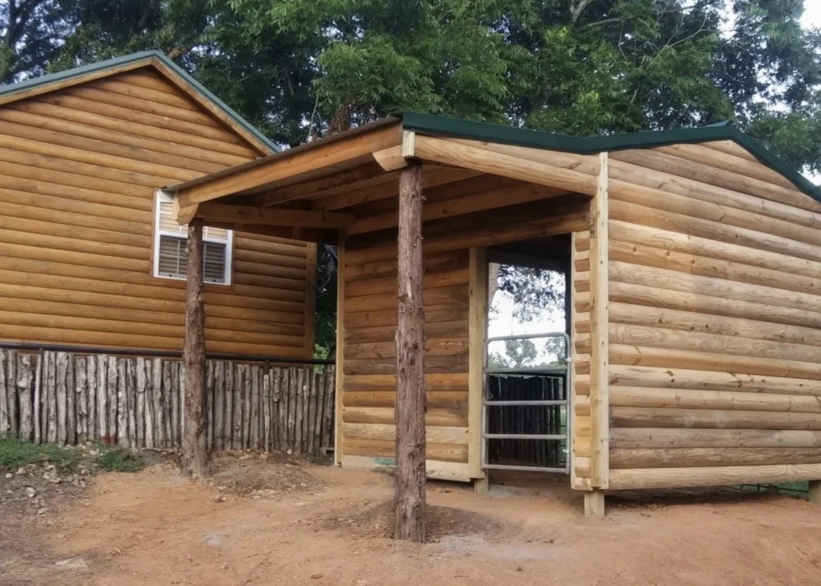 Wooden cabin with log exterior, supported by vertical logs, in a natural setting with trees.