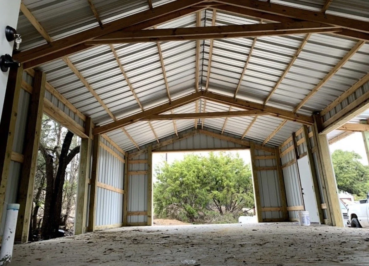 Inside of a metal garage with wooden framing, open garage door showing trees and parked vehicles outside.