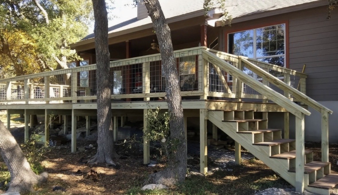 A newly built wooden deck with stairs attached to a house, surrounded by trees with autumn foliage.