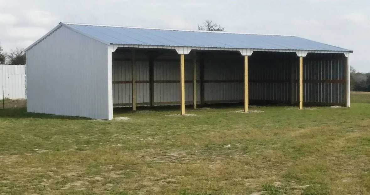 A metal carport or storage shelter with a blue roof and open sides, situated on a grassy area.