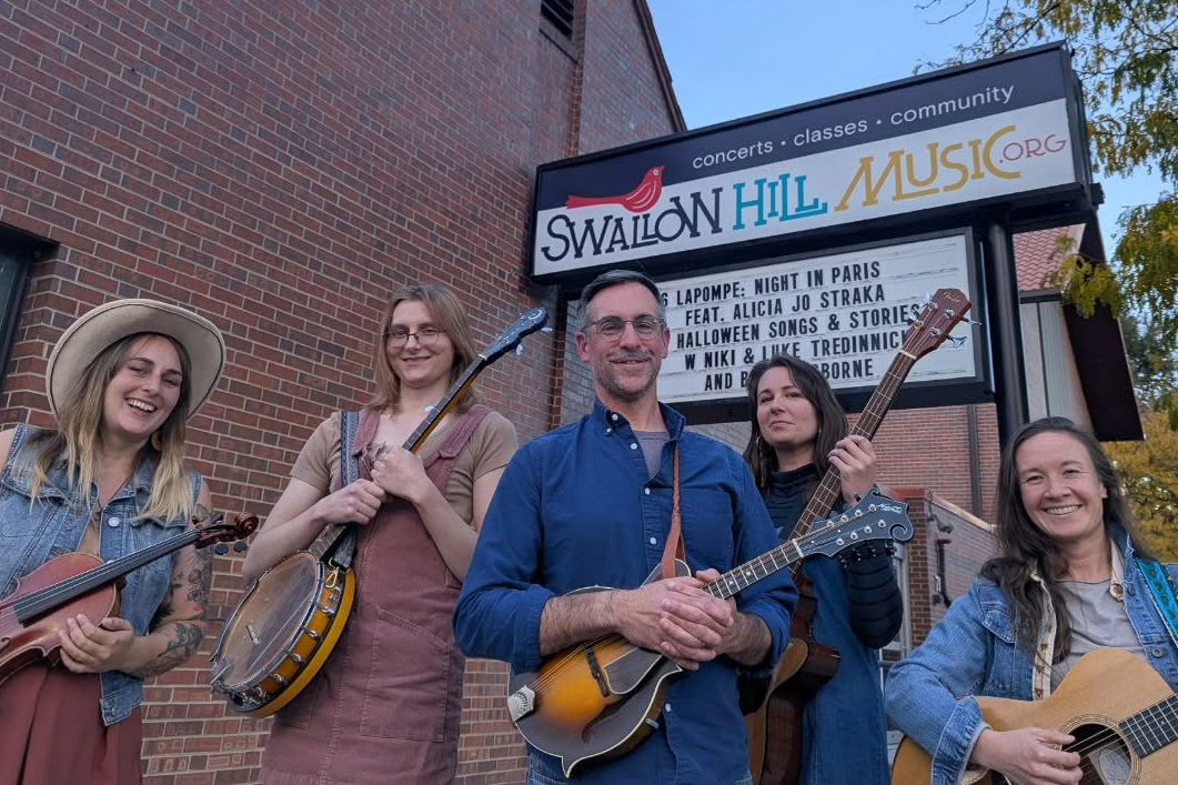 Blucifergrass, the Denver-based bluegrass band featuring Shannon Carscallen on fiddle, Elise Fatora on banjo, Mike Landis on mandolin, Julia Anderson on bass, and Anna Sours on guitar, in front of the Swallow Hill Music marquee.
