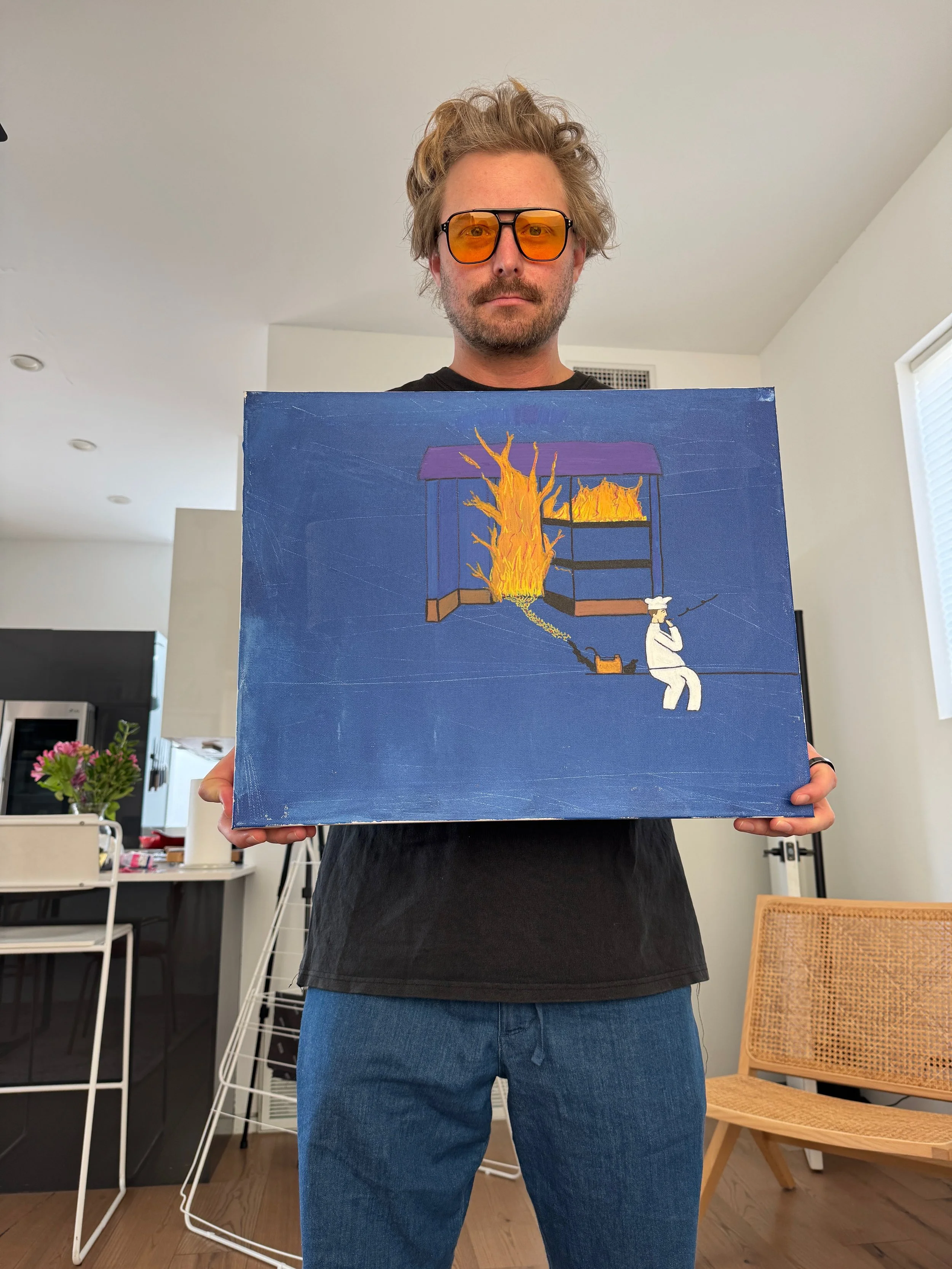A person with glasses holding a painting depicting a shop on fire, with a chef character sitting nearby, in a bright living space with furniture and a window.