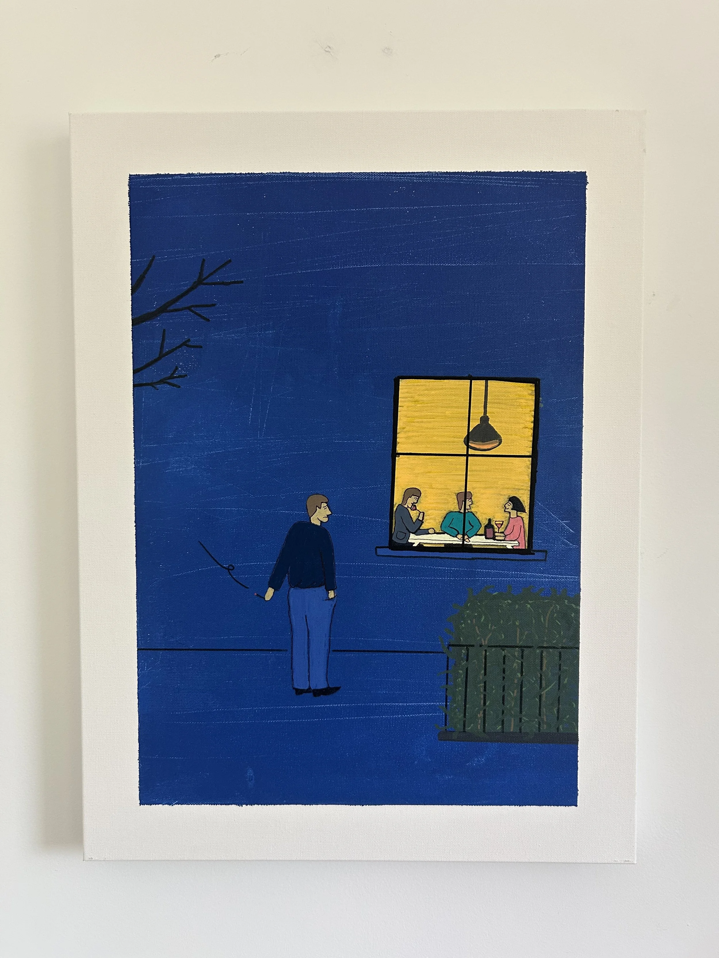 A man stands outside a lit apartment window watching strangers share dinner together.