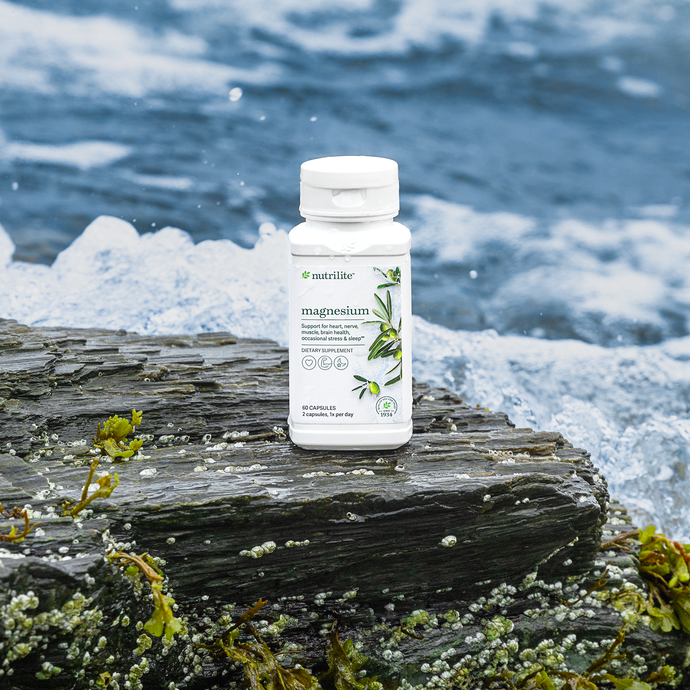 Bottle of Nutrilite magnesium supplement on a wet wooden surface near ocean waves.