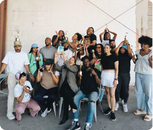 Group of diverse young people celebrating with trophies and medals outdoors against a white brick wall.