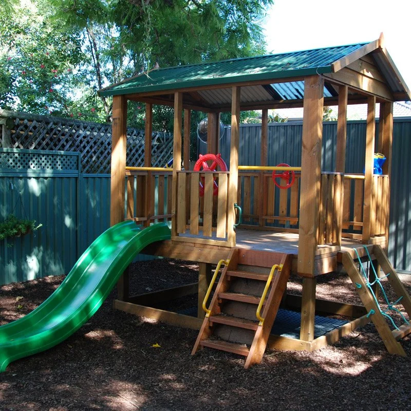 Timber cubby house with a green slide in the Bunny Cottage garden