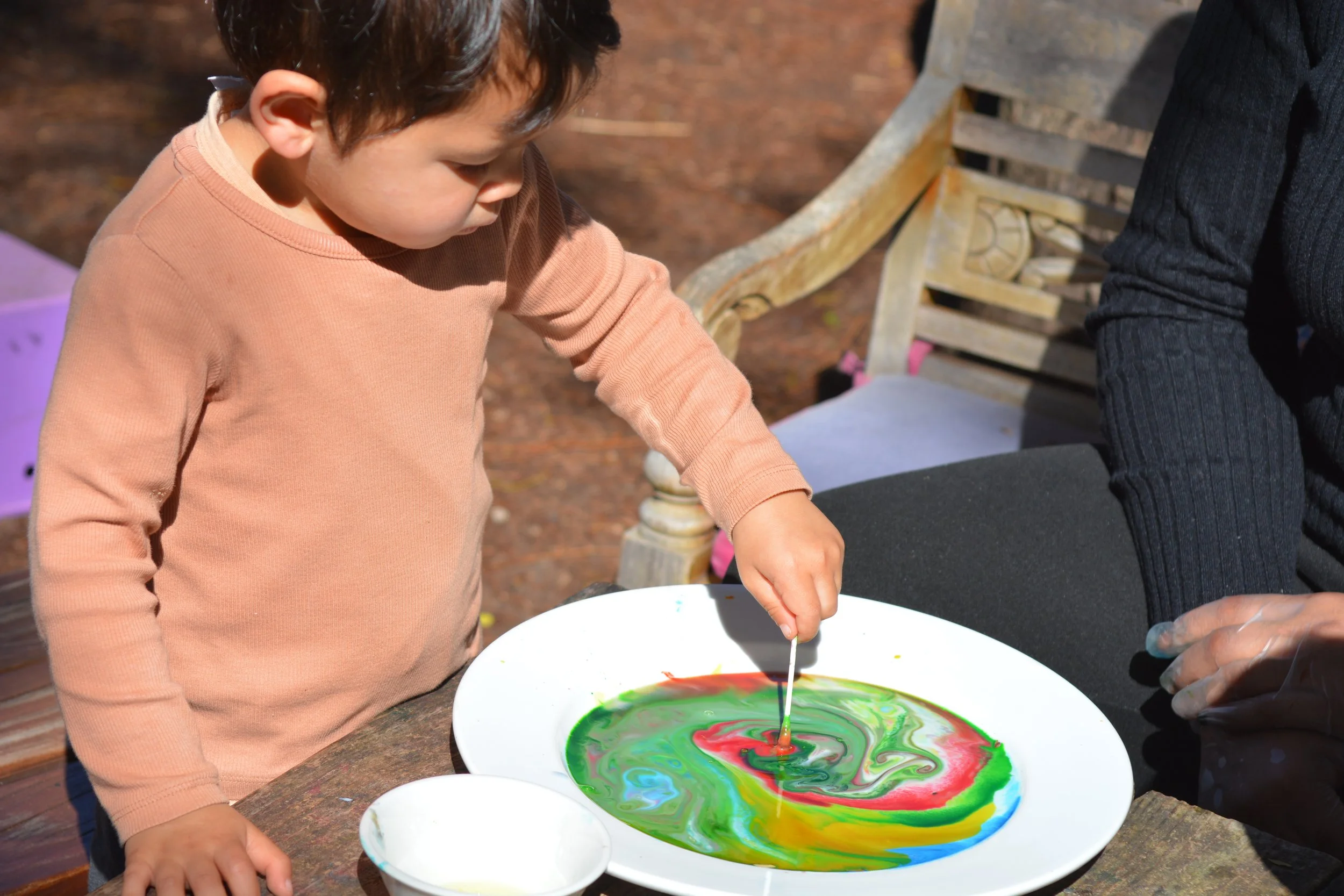 Toddler making colourful swirl art during an outdoor painting activity