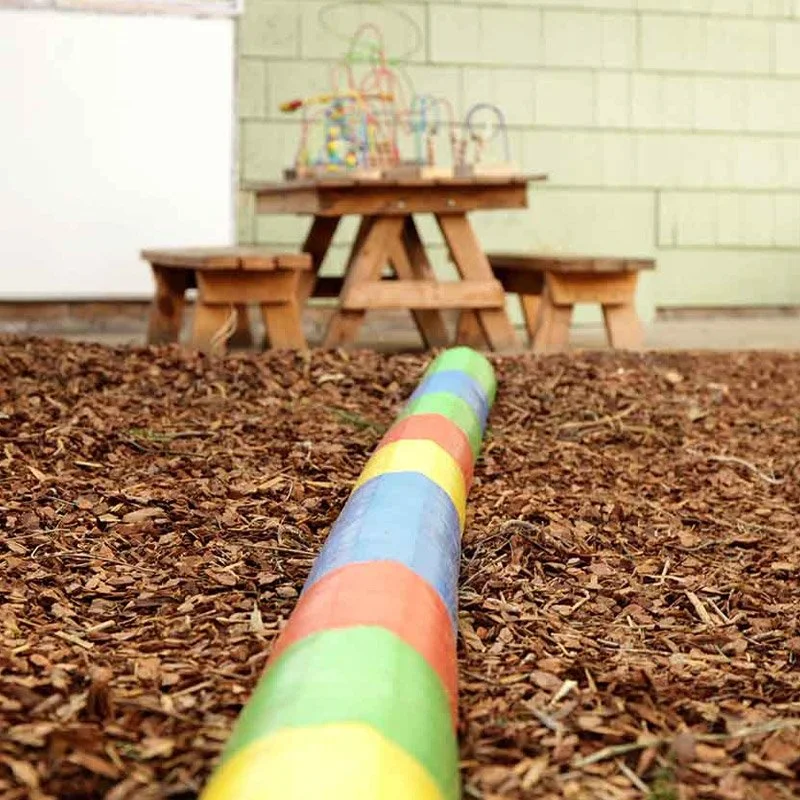 Colourful caterpillar play tunnel and timber picnic tables in the Bunny Cottage outdoor play area