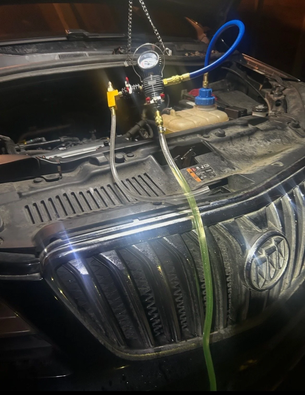 Car hood open, showing unknown device connected to the engine, possibly for maintenance or diagnostic purposes, with hoses and wires attached.